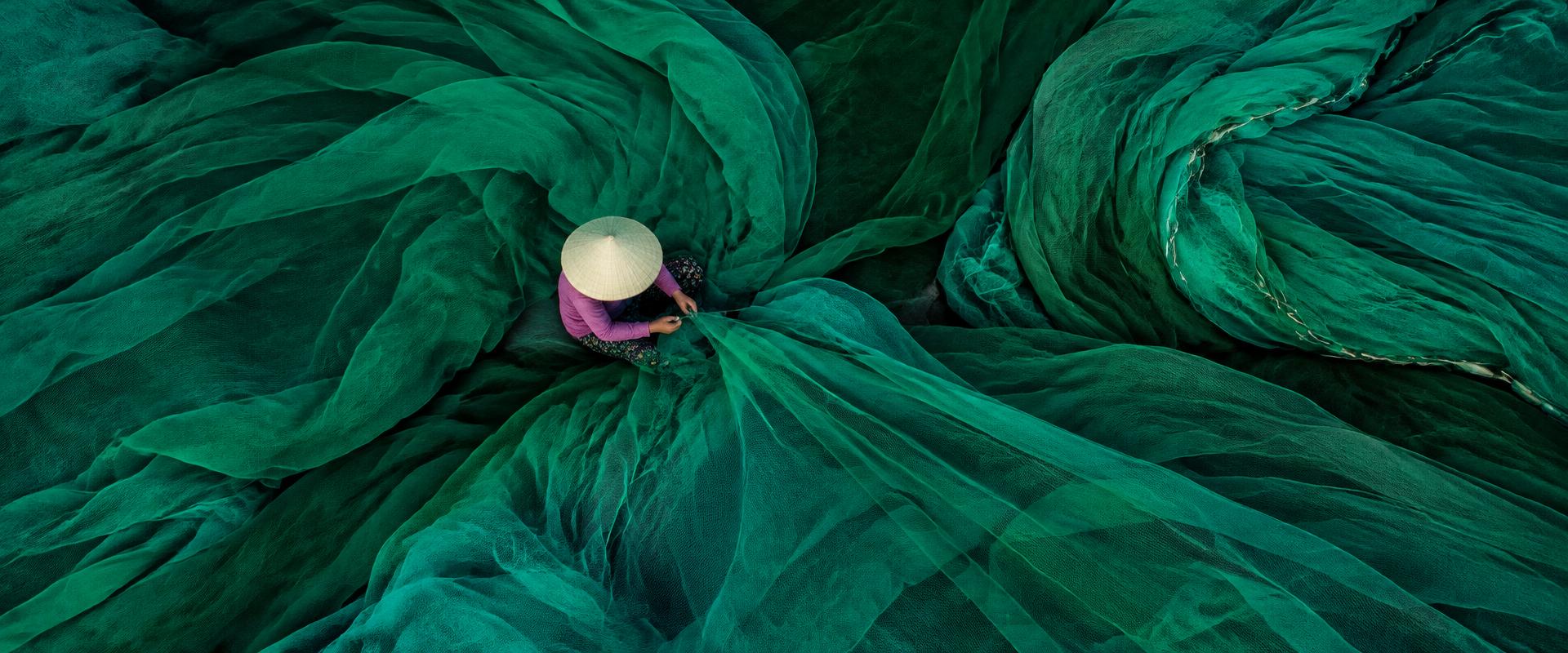 Woman mending green fishing nets in Vietnam